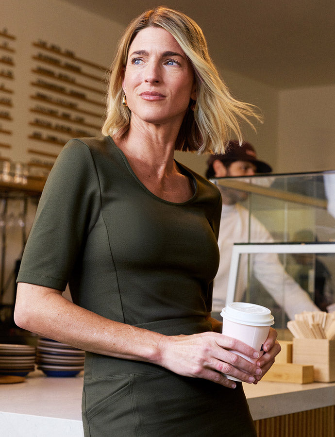 Woman wearing scrubs and holding a coffee cup.
