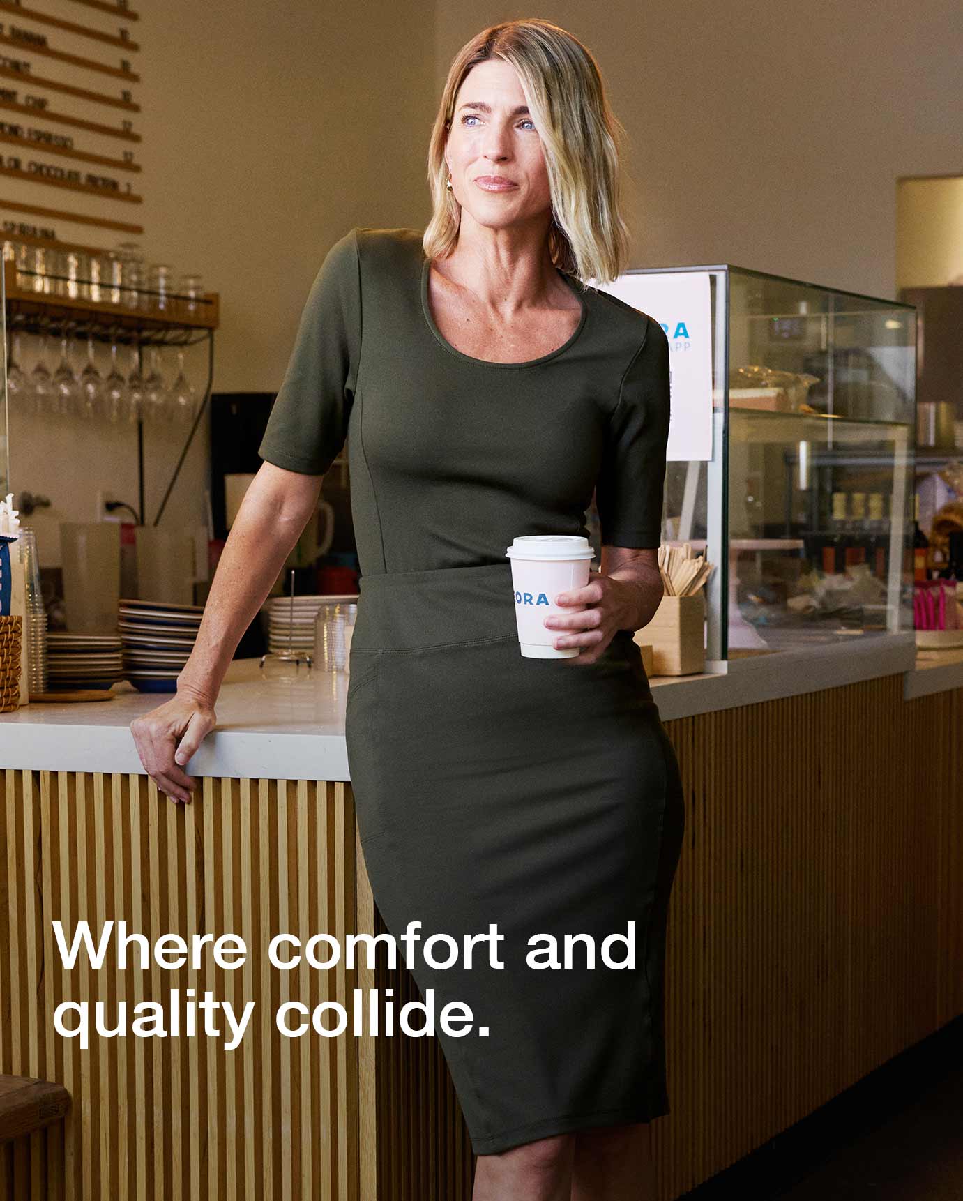 Image of woman in Deep Olive colored scrubs holding a coffee in a cafe. Image has text, "Where comfort and quality collide.".