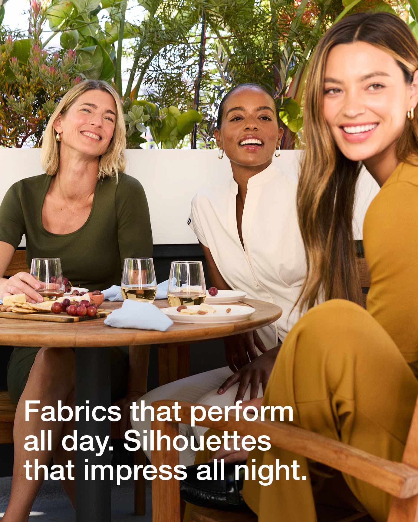 Image of 3 women wearing scrubs sitting outside at a table. Image has text, "Fabrics that perform all day. Silhouettes that impress all night."