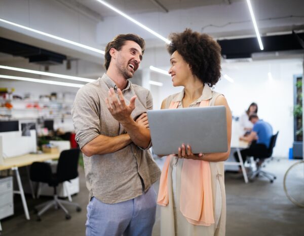 A man and a woman looking at a computer in a busy workplace.