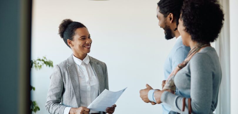 Three people stand speaking to another in an office setting.