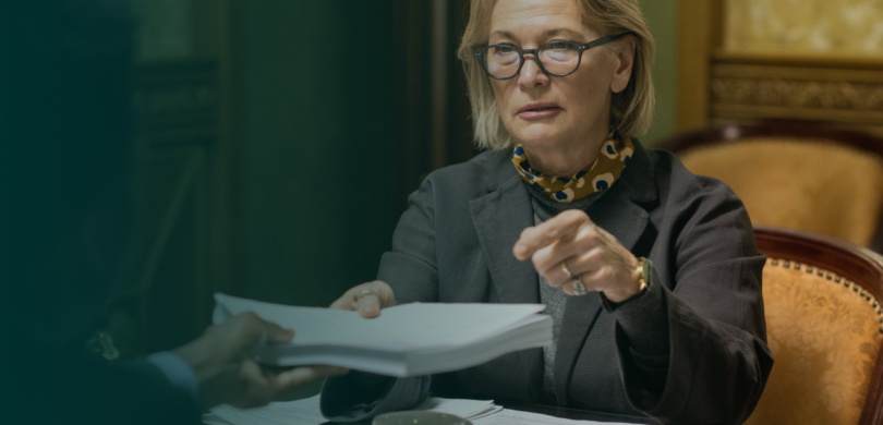 A woman sits in a business meeting surrounded by papers.