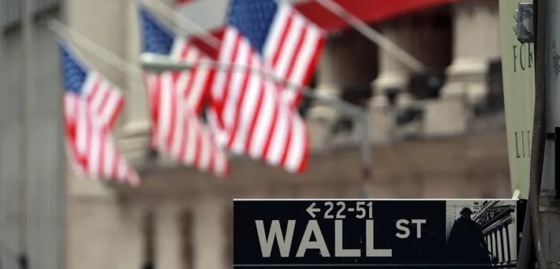Wall St. street sign with American flags in the background.